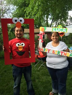 a man and woman standing in front of a house holding up a happy birthday sign