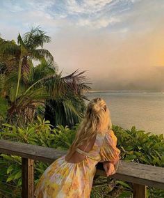 a woman sitting on a bench looking out at the water and palm trees in front of her