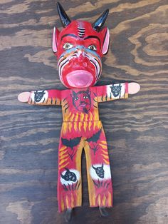 a red and yellow painted doll with horns on it's head, sitting on top of a wooden table