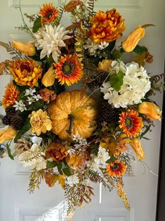 an arrangement of flowers and pumpkins is hanging on the front door for fall decor