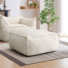 a white chair and ottoman in a room with wood flooring, potted plant and window