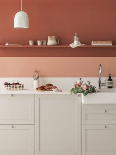 a kitchen with pink walls, white cabinets and flowers on the counter top in front of it