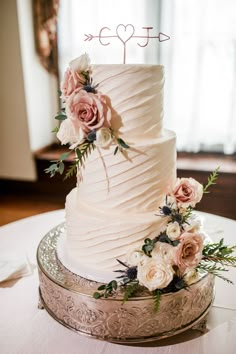 a white wedding cake with pink flowers and an arrow topper on a silver platter