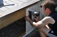 a man in black shirt using a power drill to fix a hole in the side of a house