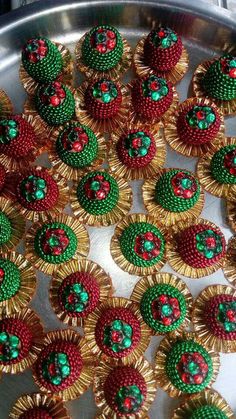 many small green and red beaded flowers on a silver tray with gold trimmings