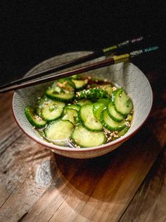 a bowl filled with cucumbers and chopsticks on top of a wooden table