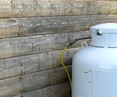 a propane tank next to a wooden wall with a yellow hose running through it