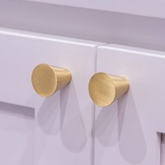 two brass knobs on the front of a white cabinet