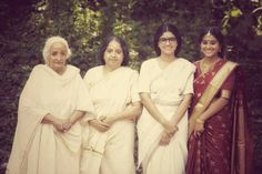 three women in white sari standing next to each other with trees in the background