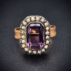 "Amethyst stones have been thought for generations to provide protection and were worn by the Ancients as a talisman for luck. The beautiful violet purple hue has also had an allure not to be resisted. Beloved by Victorians as well, it was the first color a widow was allowed to wear after coming out of mourning.  This ring was converted from an antique brooch. The beautiful, faceted rectangular amethyst is haloed by 21 natural seed pearls, which the Victorian jewelers implemented to represent \"tears of sorrow\". The faceted emerald cut amethyst stone is paired with a replica textured band, giving its new incarnation as a ring is a lovely way to showcase this classic combination of amethyst and pearl.   Details (approximate) Size: 7 Weight:  5 grams Materials: Gold, Amethyst, Seed Pearl Me Antique Oval Purple Amethyst Ring, Antique Oval Amethyst Ring, Heirloom Amethyst Ring With Accent Stones, Spiritual Oval Purple Amethyst Ring, Oval Purple Amethyst Ring With 17 Jewels, Heirloom Style Purple Amethyst Collectible Ring, Heirloom Purple Amethyst Collectible Ring, Formal Purple Amethyst Spiritual Ring, Formal Spiritual Purple Amethyst Ring