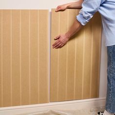 a person standing next to a wall that has been painted beige and is holding onto the paneling