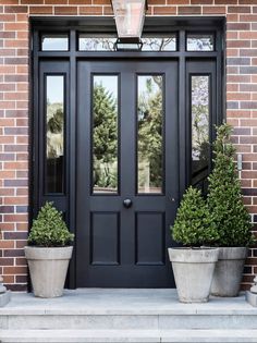 two planters are on the front steps of a house with black doors and windows