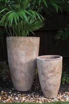 two large cement pots sitting next to each other on top of a gravel covered ground