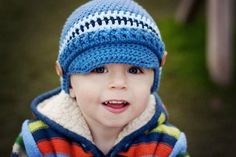 a young boy wearing a blue crocheted hat and striped jacket smiling at the camera