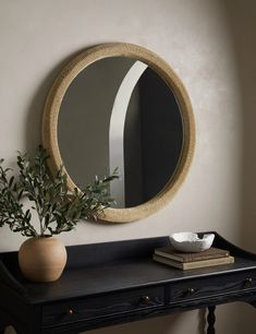 a round mirror sitting on top of a wooden table next to a vase filled with plants