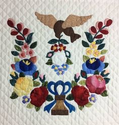 a quilted wall hanging with flowers and two birds on it's back side