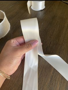 a person holding a white ribbon on top of a wooden table next to two rolls of tape