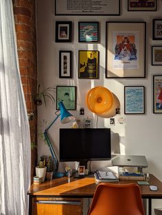 a desk with a computer on top of it next to a wall full of pictures