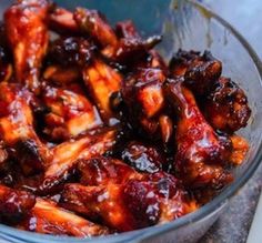 a glass bowl filled with chicken wings covered in bbq sauce on top of a table