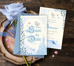 two blue and white wedding cards on a plate next to a pink rose with ribbon