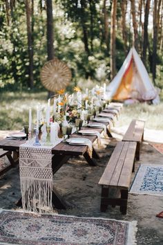 a long table with candles and flowers on it in the middle of a wooded area