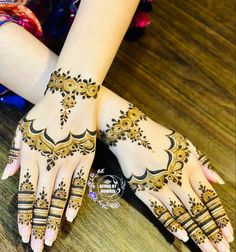 two hands with henna tattoos on them sitting on a wooden table in front of a woman's hand