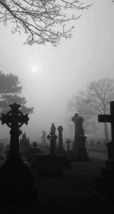 a cemetery with tombstones and crosses in the fog