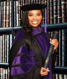 a woman in a purple graduation gown holding a book and a black cap on her head