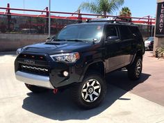 a black toyota 4runner is parked in front of a sign and some palm trees