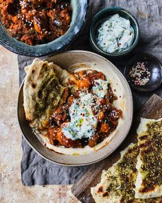 some food is sitting on a table next to other dishes and utensils, including pita bread