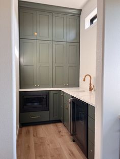 an empty kitchen with green cabinets and white counter tops, wood flooring in the foreground