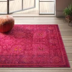 a pink area rug with an orange pouffle on the floor in front of a window