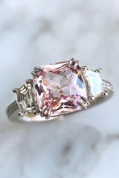 a pink and white ring with three baguets on it's sides, sitting on a marble surface