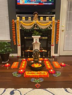 a decorated fireplace with candles and flowers on the floor in front of it is a television