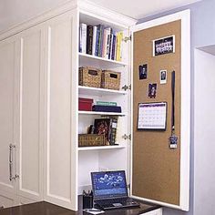 a white cabinet with a laptop on top of it and a corkboard wall behind it