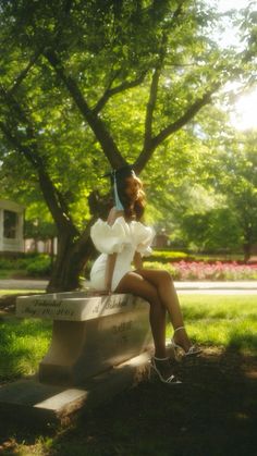 a woman sitting on top of a bench under a tree