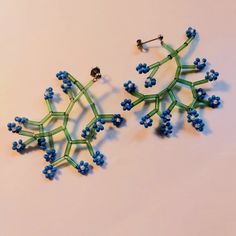 a pair of earrings made out of green and blue beads on a white surface with one beaded snowflake in the middle