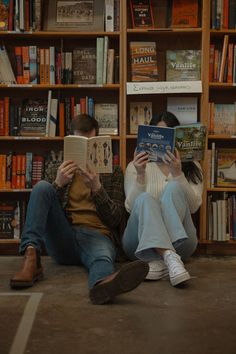 two people sitting on the ground reading books in front of a book shelf full of books