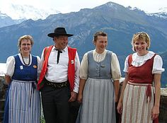 three women and two men are standing in front of a scenic mountain view with mountains behind them