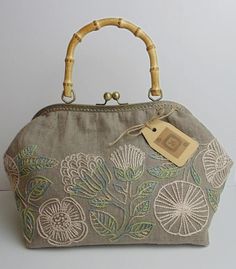 a handbag with an embroidered design on the front and bamboo handle, sitting on a white surface