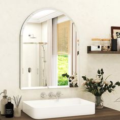 a white sink sitting under a bathroom mirror next to a vase with flowers in it