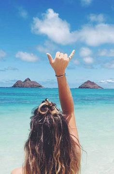 a woman standing on top of a beach next to the ocean holding her hands up