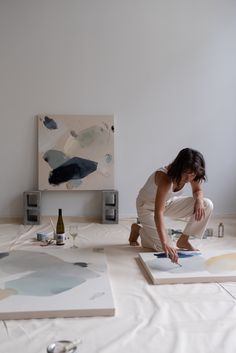 a woman kneeling down on the floor in front of two pieces of art that are being displayed