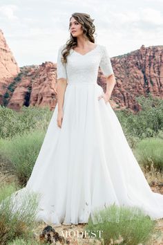 a woman in a white wedding dress standing on the side of a mountain with her hands on her hips