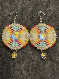 a pair of colorful beaded earrings on top of a gray surface with silver earwires