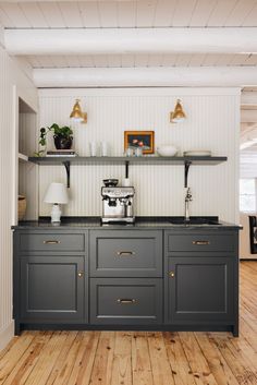 a kitchen with wooden floors and white walls, two coffee machines on top of the cabinets