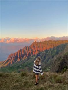 a woman walking up a hill with mountains in the background