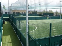 an outdoor tennis court with green grass and fenced in areas around the perimeters