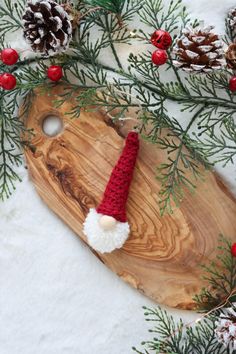 a wooden cutting board with a santa hat on it next to pine cones and evergreen needles