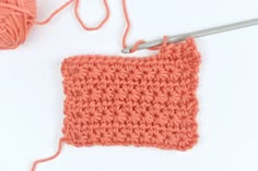 an orange crochet square is next to a ball of yarn and a pair of scissors